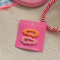 Detail view of wavy candy-colored hair clips in pink and orange on a display card - Orange and Pink