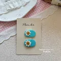 Détail de barrettes brodées de marguerites bleues pour enfants sur une assiette décorative - Barrettes Fleur Ovale Bleues
