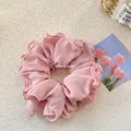 Détail du chouchou plissé rose clair avec bords ondulés sur un fond texturé doux - Rose