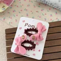 Dettaglio di due fermagli per capelli a fiocco rosa con pon pon marroni su carta - Gold Label Style / Stile Fiocco Etichetta Oro Rosa