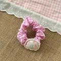 Dettaglio di elastico per capelli a quadretti rosa con patch pecora su sfondo rustico - Elastico Rosa