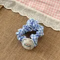 Dettaglio di scrunchie a quadretti blu con ciondolo a gatto su lino rustico - Elastico Blu