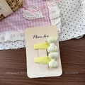 Détail de deux barrettes à nœuds rayés jaunes sur carton naturel avec un décor rustique - Barrette à Nœud Jaune