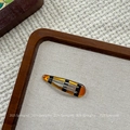 Detail view of a translucent amber tortoiseshell BB hair clip on a wooden tray - Amber Waterdrop BB Clip (NK2084-5)