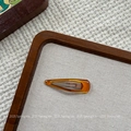 Close-up of a minimalist amber resin hair clip on a textured woven fabric background - Yellow Brown Solid Waterdrop BB Clip (NK2084-7)