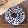 Detailed shot of blue gingham scrunchie with pink wavy edges and white floral brand label - Blue Checkered Fabric