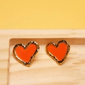Detailed view of orange enamel heart stud earrings with gold textured edges on a wooden tray - Orange