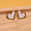 Macro shot of gold heart earrings with white inlay and hammered texture on wood tray - White