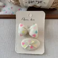 Détail de barrettes en tissu à imprimé cœur avec nœud et perle sur présentoir - Pince à Cheveux Imprimé Nœud Papillon