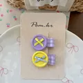 Detalle de pinzas para el cabello con botones y lazos en tarjeta de presentación - Púrpura y Amarillo