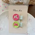 Detalle de horquillas de botón rosa y verde con lazos en tarjeta de muestra en un bol blanco - Rojo Rosa y Verde