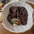 Dettaglio di un elastico marrone con ciondolo a fungo in peluche in un cesto di vimini - Marrone
