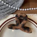 Close-up of leopard print plush hair claw clip on a ceramic tray with warm textures - Leopard Print Shark Clip