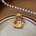 Dettaglio del fermaglio per capelli ricamato con orsetto e cuore su piatto decorato - Pezzo Singolo / Orso con Salopette Gialla