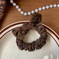 Dettaglio dell'elastico scrunchie maculato con fiocco decorativo su un piatto - Scrunchie con Fiocco / caffè