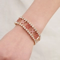 Detailopname van een goudkleurige XOXO armband met rode en roze strass op de pols - Opengewerkte Letters Armband (BS-J5478G)