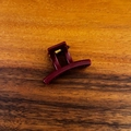 Detailweergave van een wijnrode kleine haarklem met een gouden metalen veer op hout - Rood