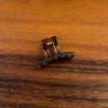 Macrodetail van de amberkleurige mini haarklem met gouden veer op houten achtergrond - Theegrijs