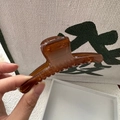 Primo piano di una clip per capelli marrone traslucido di 12 cm tenuta in mano per scala - Caffè Gelatina