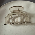 Top view of a large brown pumpkin claw clip on a textured white plate with metal spring - Transparent Tea