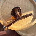 Macro detail of amber tortoise hair claw clip with wooden texture on a wooden tray - Painted Caramel Coffee