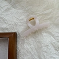 Detalle de pinza de resina rosa claro con muelle dorado sobre fondo blanco texturizado - Blanco