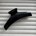 Close-up of glossy black hair claw clip with elegant minimalist curved design on beige texture - Black