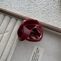 Top view of a glossy burgundy shark hair claw clip on a beige velvet jewelry tray - 3D Cross Twisted Style / Burgundy