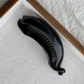 Close-up of a glossy black banana hair clip with fine teeth on grey fabric background - Black