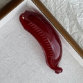Macro shot of dark red glossy banana hair clip with secure inner teeth in a tray - Red