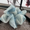 Detail eines blau-weißen Chiffon-Scrunchies mit Tintentextur auf einem Holztisch - Blauer Tuschewaschgang