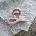Detalle de la pinza de pelo rosa palo con muelle dorado sobre papel blanco rugoso - Rosa