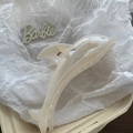 Detalle de pinza para pelo de delfín blanco perla con muelle de metal dorado sobre fondo textil - Delfín Blanco