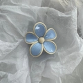Close-up of a light blue flower hair claw clip with glossy resin petals on white paper - White Edge Blue Flower