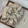 Close-up of a plaid hair scrunchie with pink ruffle edges and cute cartoon dog patterns - Beige