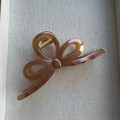 Detail of a large bow-shaped hair claw with an amber iridescent pearlescent finish - Brown