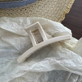 Close-up of cream rectangular hair claw clip with glossy finish and gold metal spring - Off White