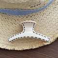 Detalle de una pinza para el cabello crema con costuras negras sobre un sombrero - Blanco