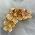 Detailed macro view of yellow marble acetate frangipani hair claw clip on soft fabric - Triple Flower Row Shape