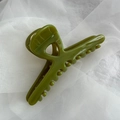 Detail view of olive green glossy hair claw clip on white mesh fabric background - Green