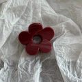 Macro detail of glossy dark red flower-shaped hair claw clip on white textured paper - Solid Red