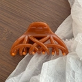 Dettaglio macro di un grande fermaglio per capelli in resina ambrata con motivo intrecciato - Caffè Gelatina
