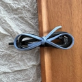 Detail der hellblauen Wildleder-Schleife und glänzenden schwarzen Haarklammer auf Holz - Blau Wildleder Schleife