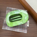 Vue détaillée d'une grande pince à cheveux marbrée verte sur un bureau rétro boisé - Vert