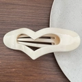 Dettaglio macro della molletta per capelli a forma di cuore color crema su sfondo neutro - Bianco Solido