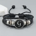 Close-up of multilayer black leather bracelet with letter G charm and metal beads - Letter G