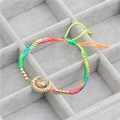 Detail eines bunten geflochtenen Armbands mit goldenem Mondanhänger und Mikro-Zirkonia - Biene