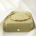 Dettaglio di un bracciale aperto dorato a forma di bambù su una scatola di velluto verde - Oro