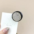 Close-up of small round hair claw clip with pavé rhinestones on black base and gold trim - Round Black White Stone