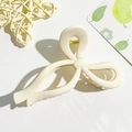 Detail of a creamy white bow hair claw clip with a glossy finish and golden spring - Cream Bow Style